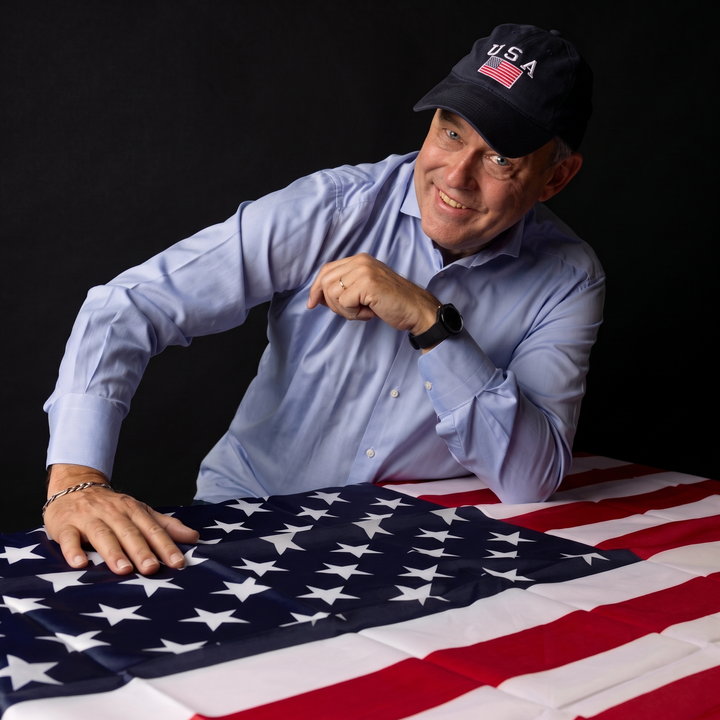 Charles Groenhuijsen met een USA-pet, leunend op een Amerikaanse vlag